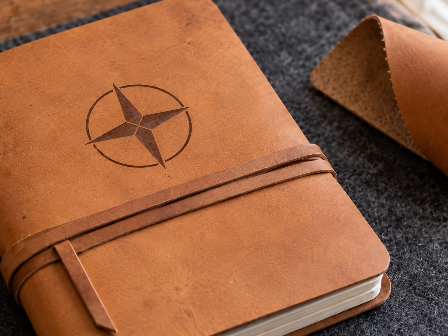 Close view of the same flat compass marking across the leather grain, beside the journal strap and rounded cover edge