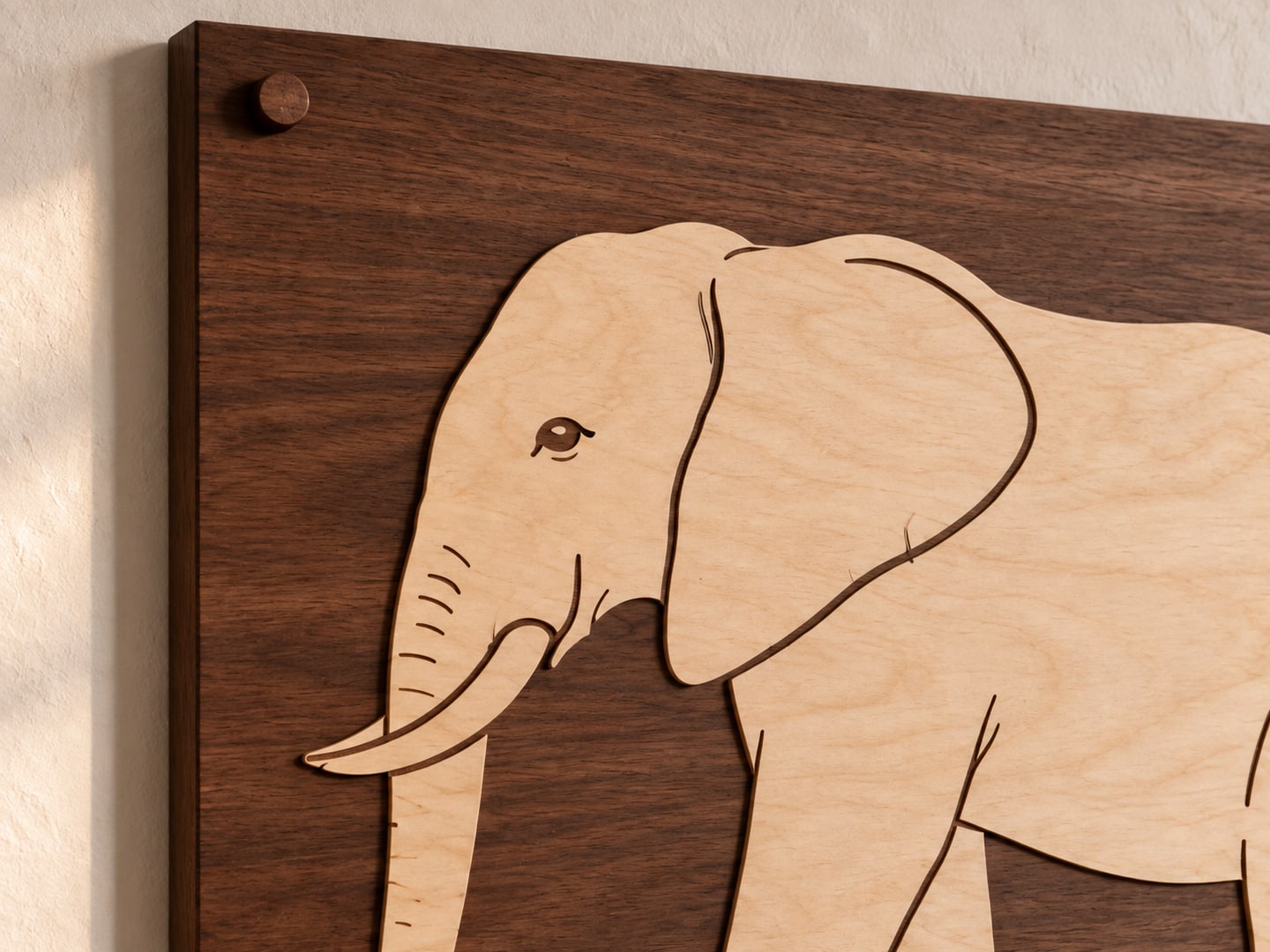 Close view of a continuous pale birch elephant silhouette on a solid walnut board, with its eye and ear outline engraved into the pale wood